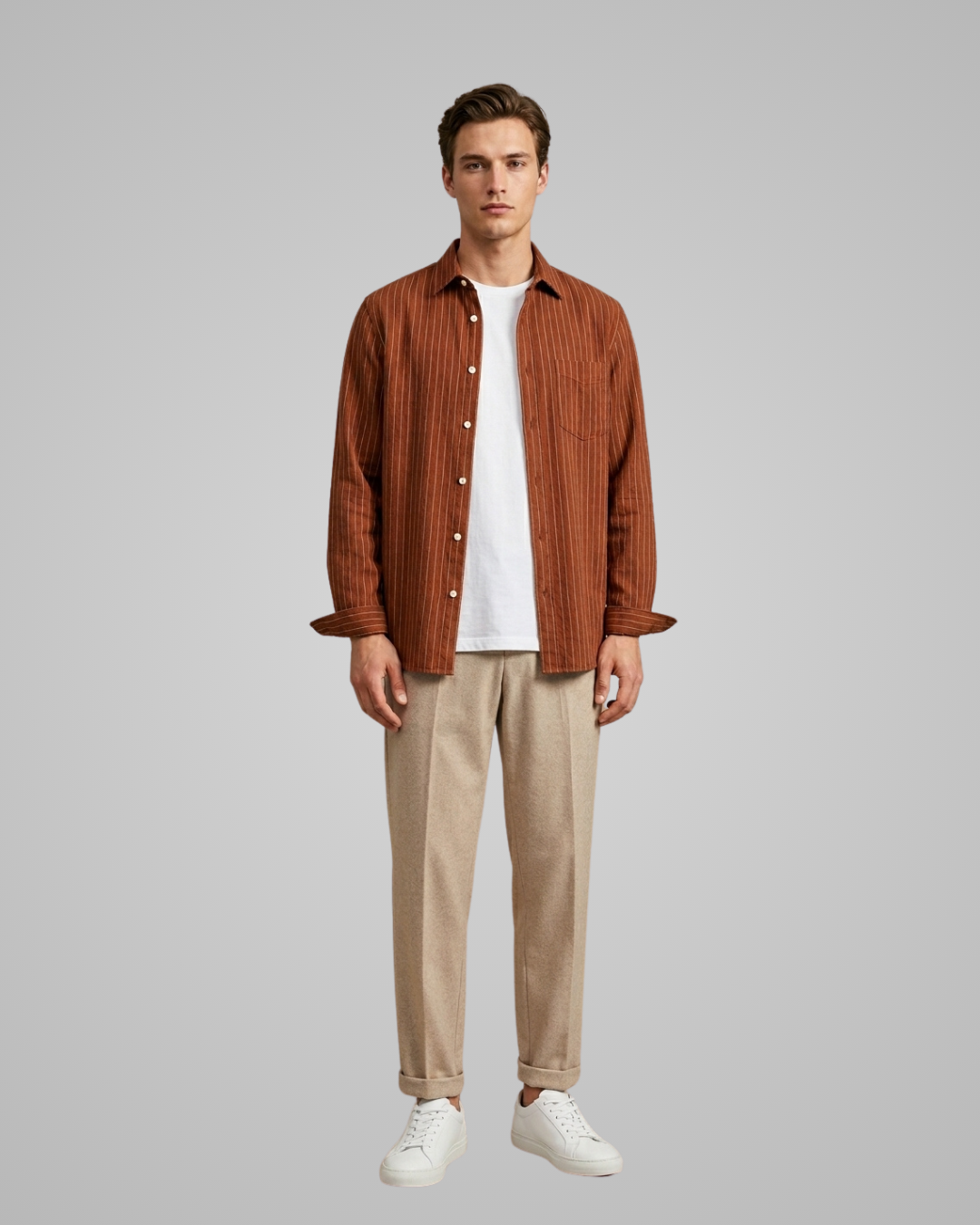 Man wearing a brown corduroy shirt, white t-shirt, beige pants, and white sneakers on a gray background