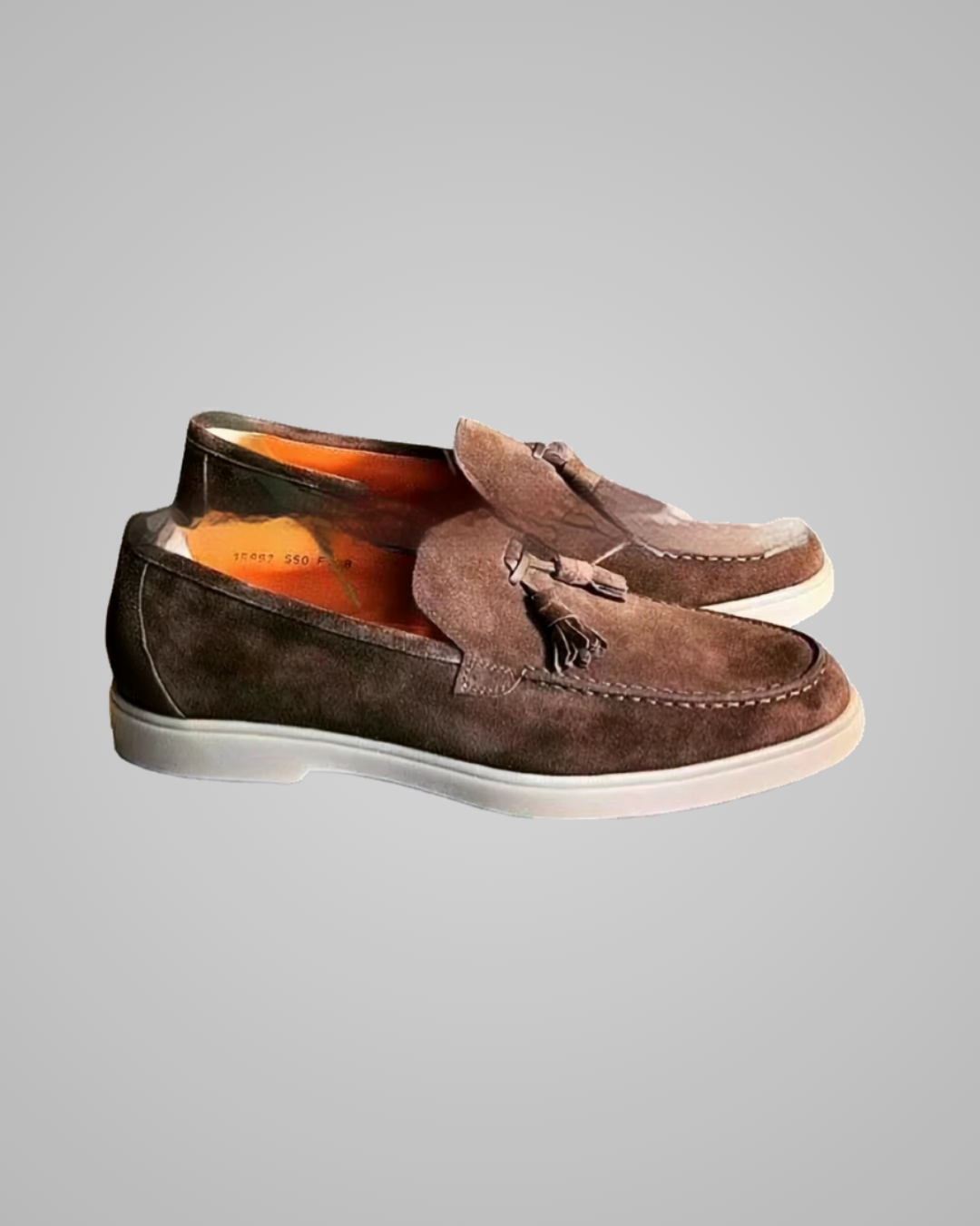 A pair of brown suede tassel loafers with white soles, shown from a side profile view against a solid gray background.