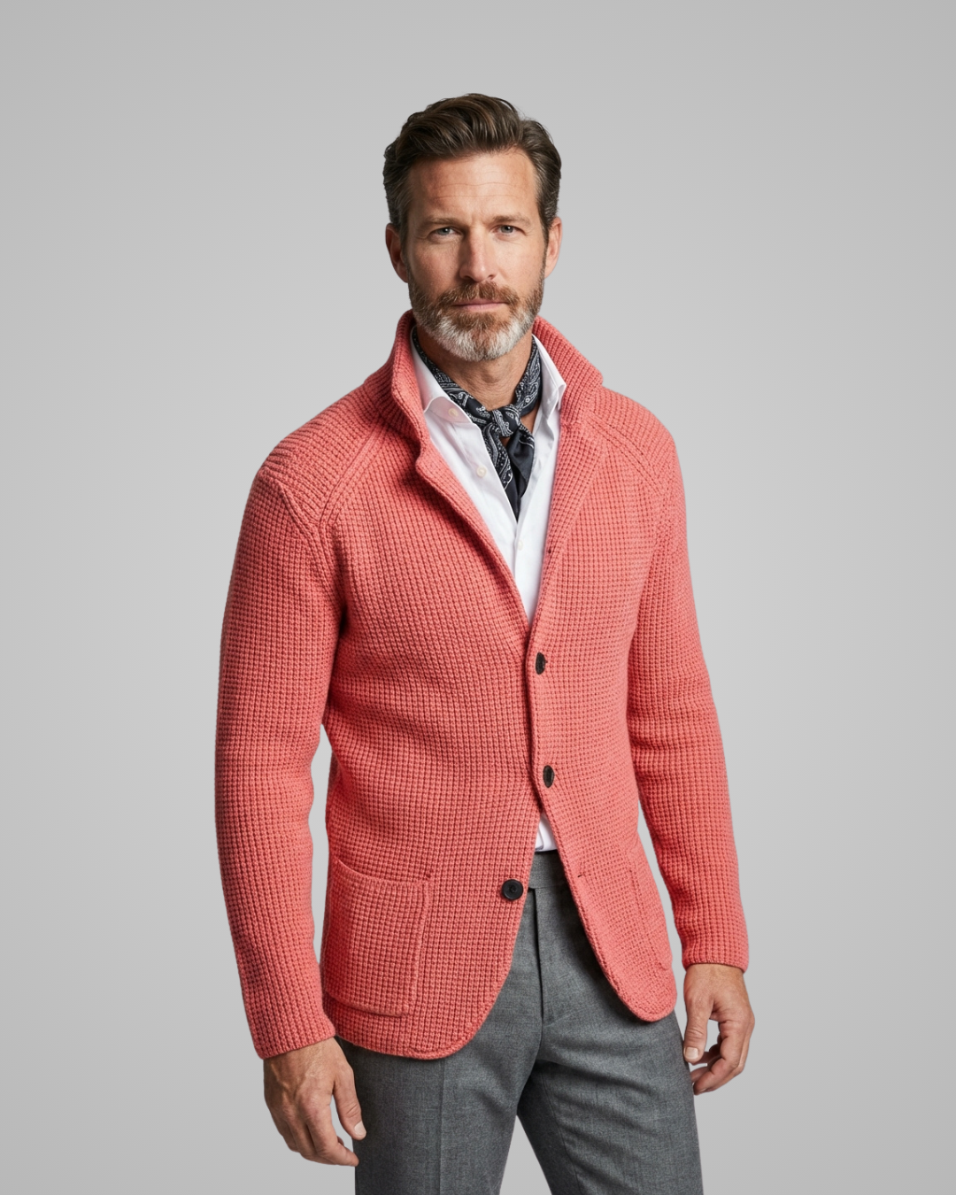 Man wearing a coral cardigan over a patterned shirt with gray pants on a gray background