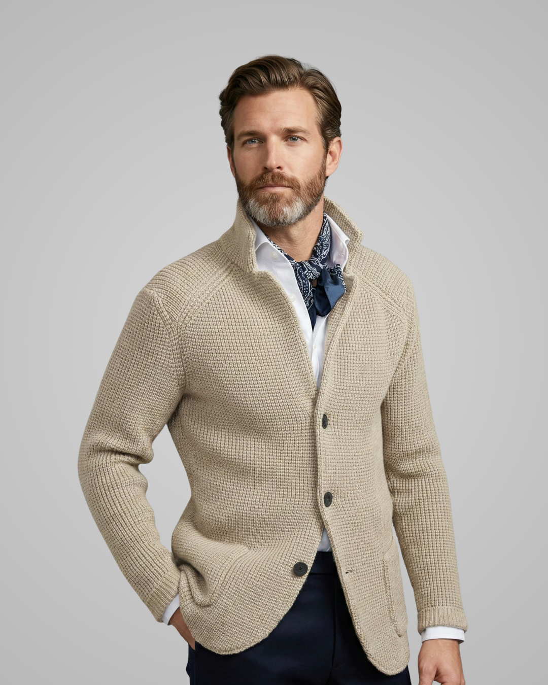 Man wearing a beige cardigan over a patterned shirt with a gray background