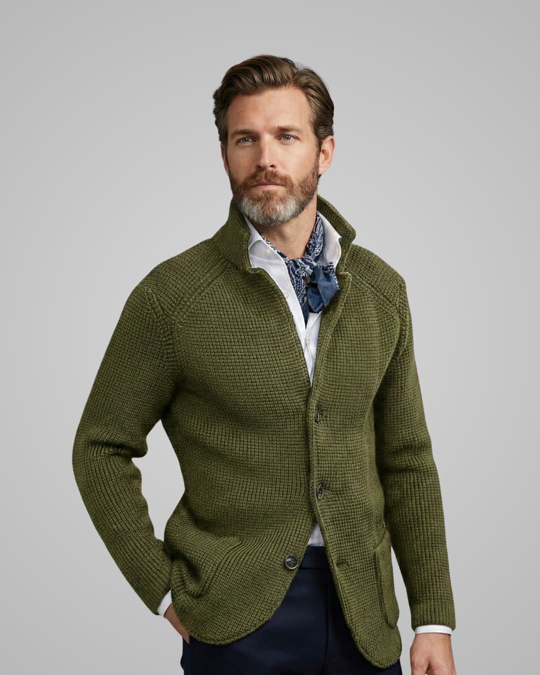 Man wearing a green knitted cardigan over a white shirt with a blue patterned scarf, on a gray background.