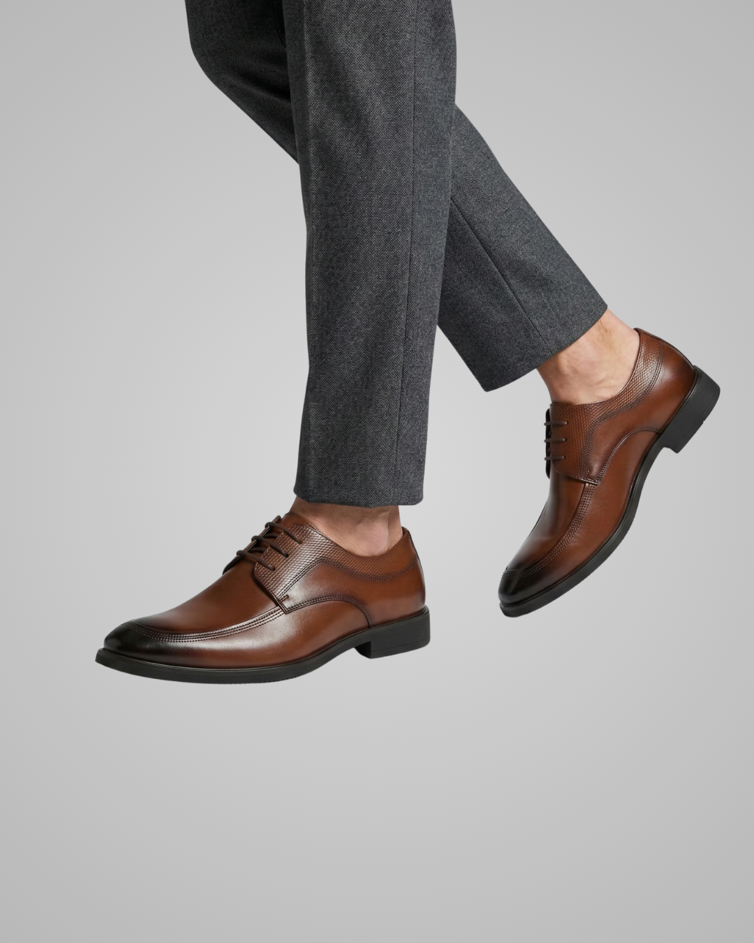 Brown dress shoes worn with gray pants on a light gray background
