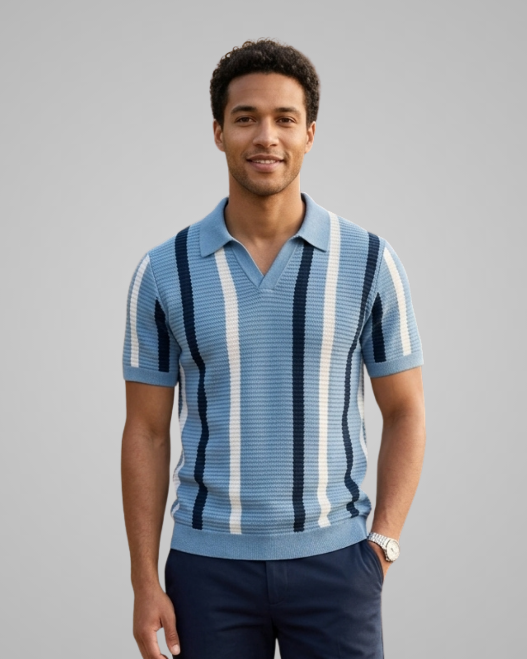 A man wearing a light blue and white vertically striped knit polo shirt with navy blue pants, standing against a solid gray studio background.