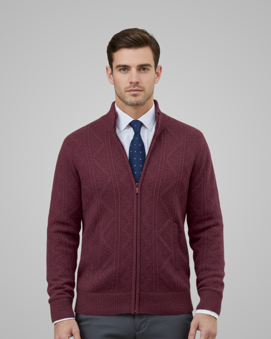 Man wearing a burgundy sweater over a white shirt with a blue patterned tie on a gray background