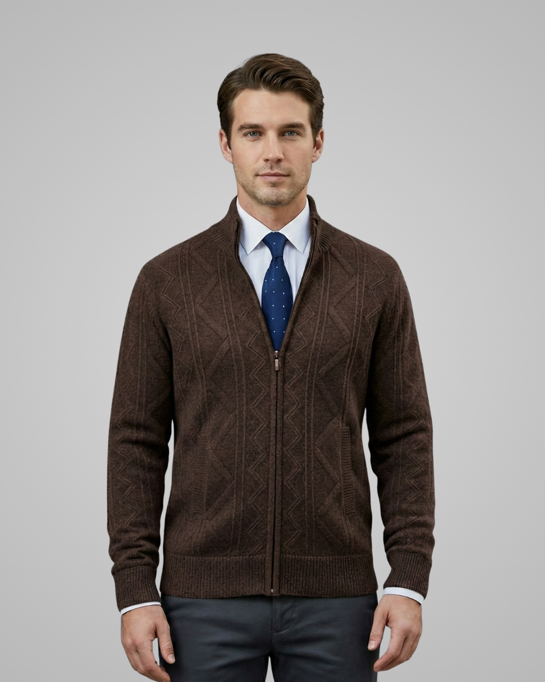 Man wearing a brown zip-up sweater over a white shirt with a blue patterned tie on a gray background