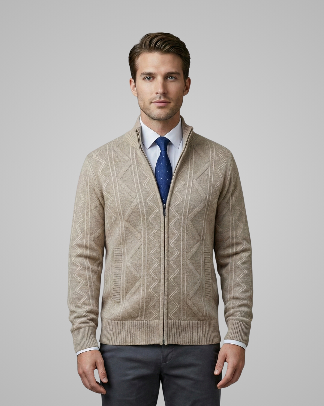 Man wearing a beige patterned sweater over a white shirt with a blue tie, on a plain background