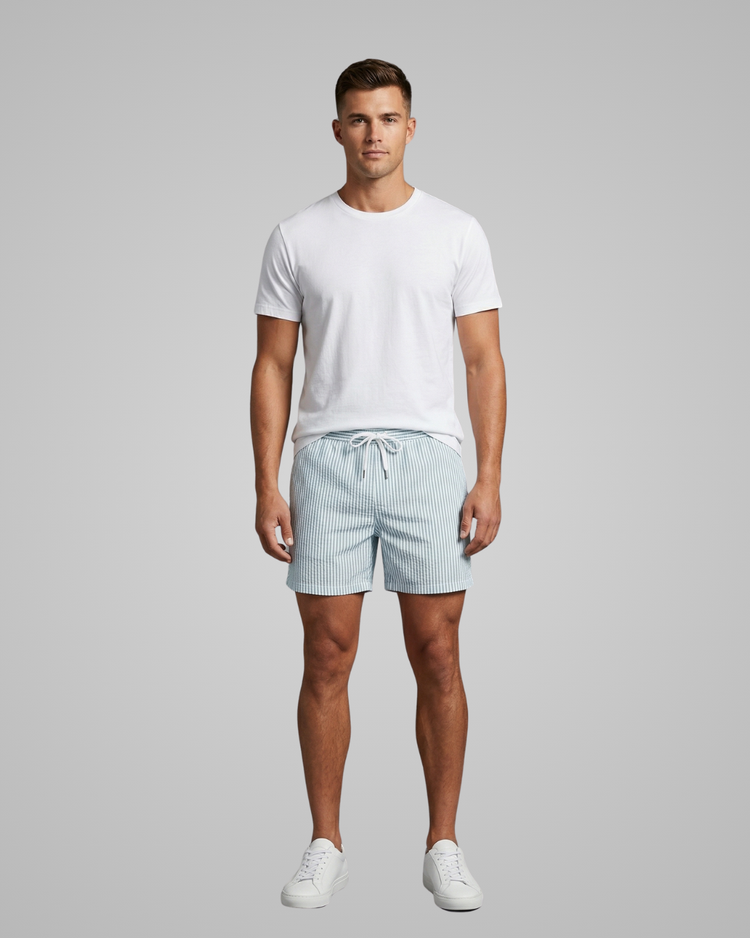 Man wearing a white t-shirt and light blue striped shorts on a gray background