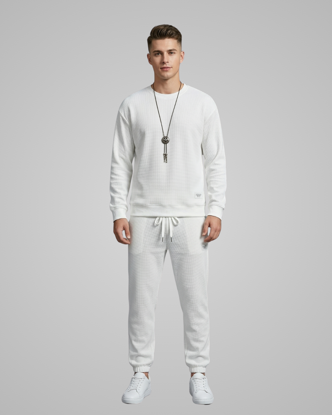 Man wearing a white sweatshirt and pants with a necklace on a gray background