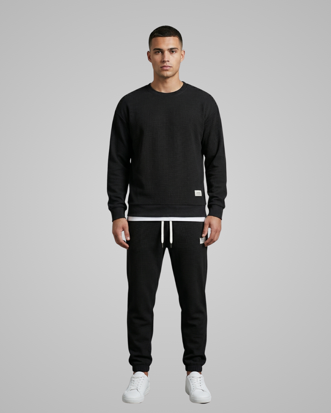 Man wearing a black sweatshirt and pants with white accents on a gray background