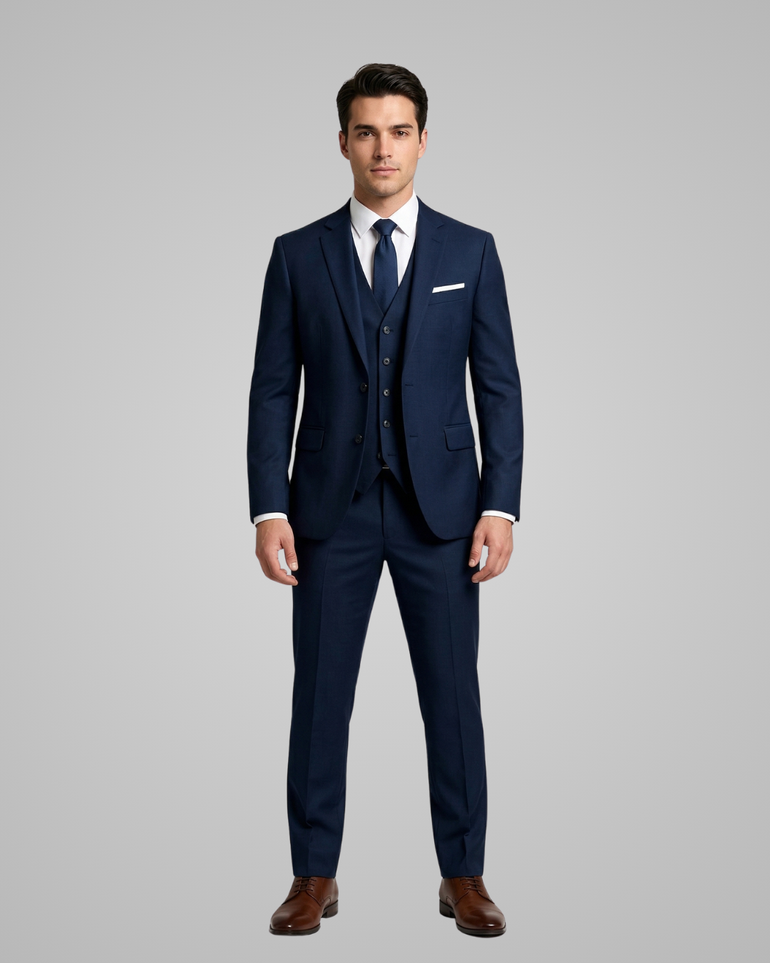 Man wearing a navy blue suit with a white shirt and brown shoes on a gray background