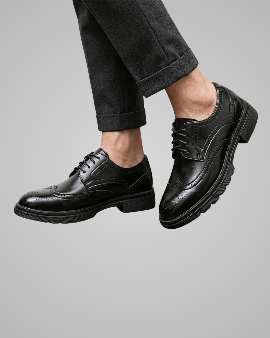 Black dress shoes worn with rolled-up gray pants on a gray background
