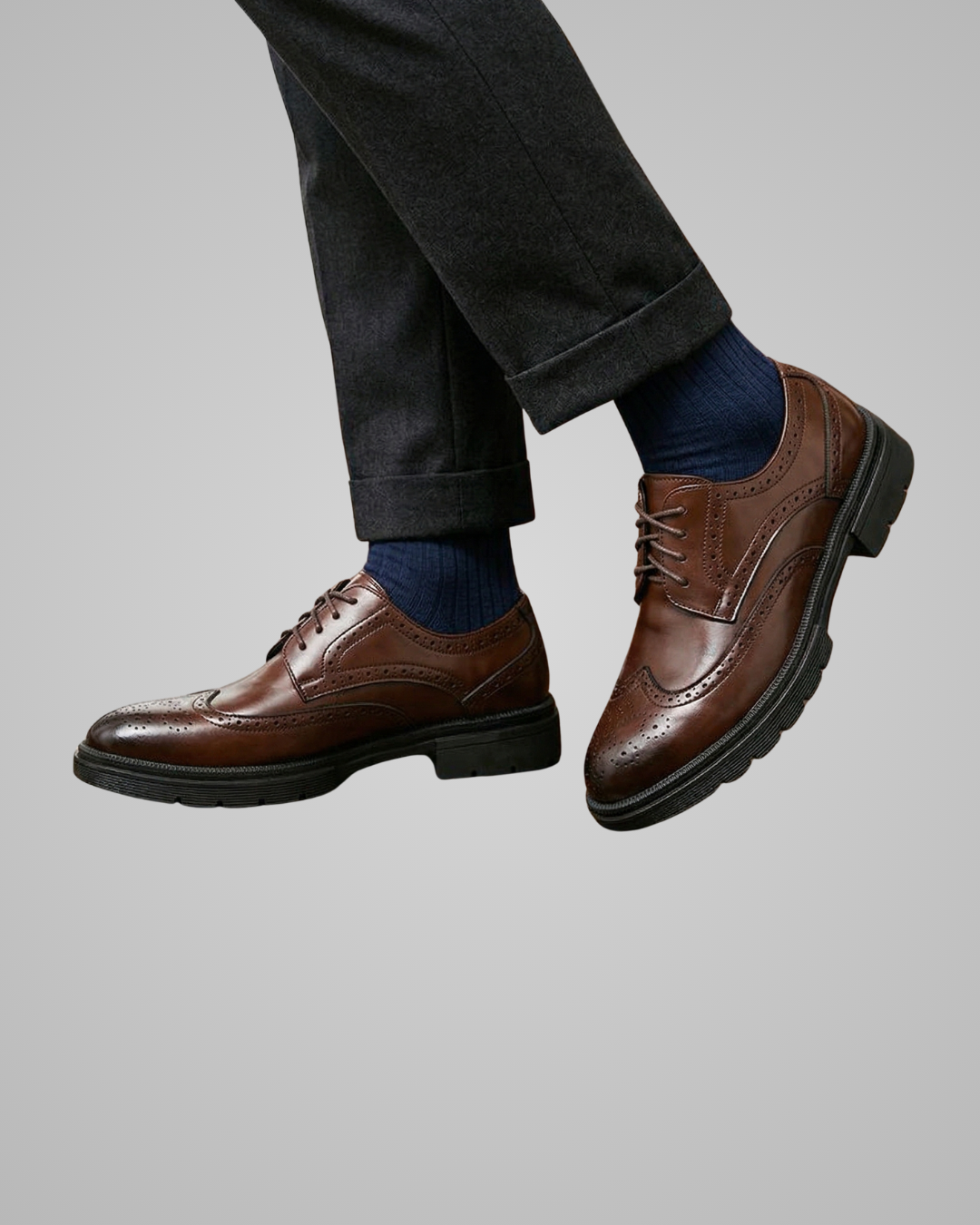 Brown dress shoes worn with dark pants and blue socks on a gray background