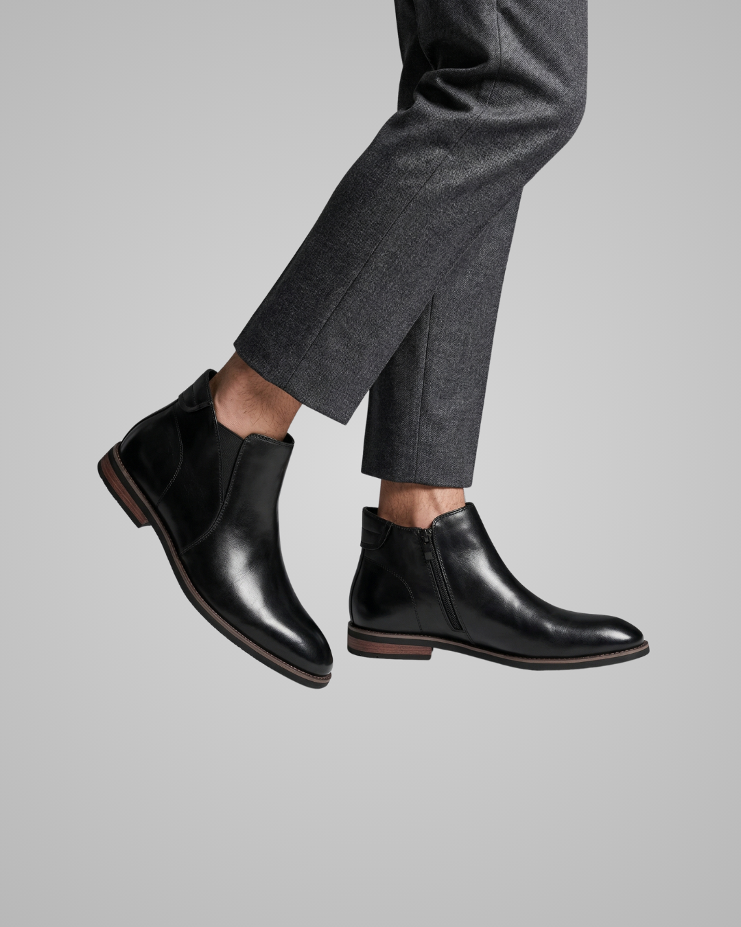 Black leather boots worn with gray trousers on a light gray background