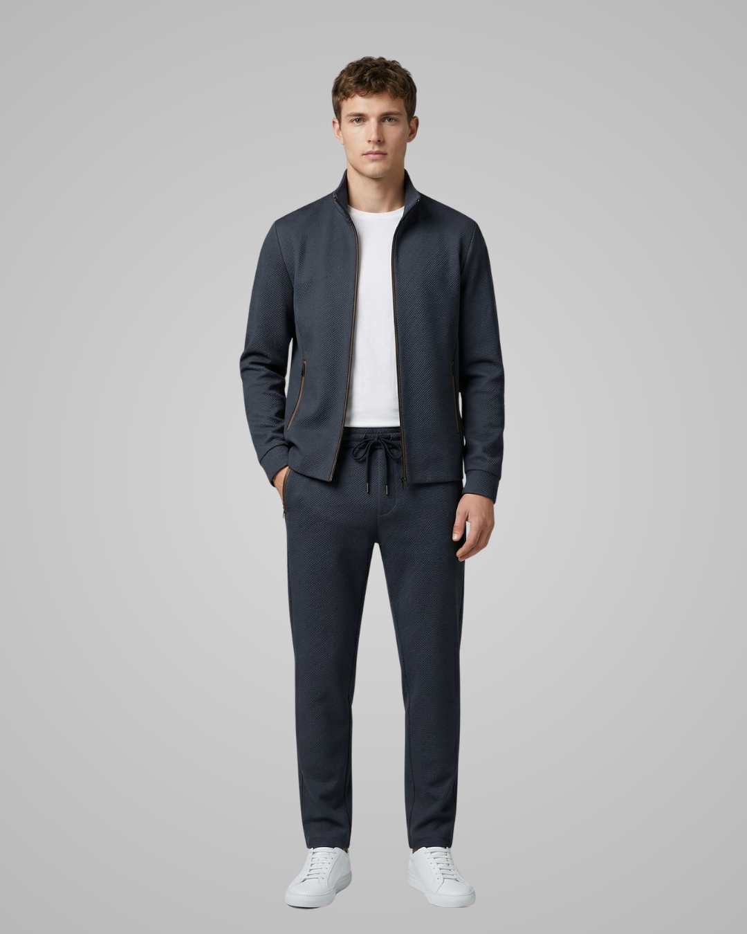 Man wearing a navy tracksuit with a white shirt on a gray background