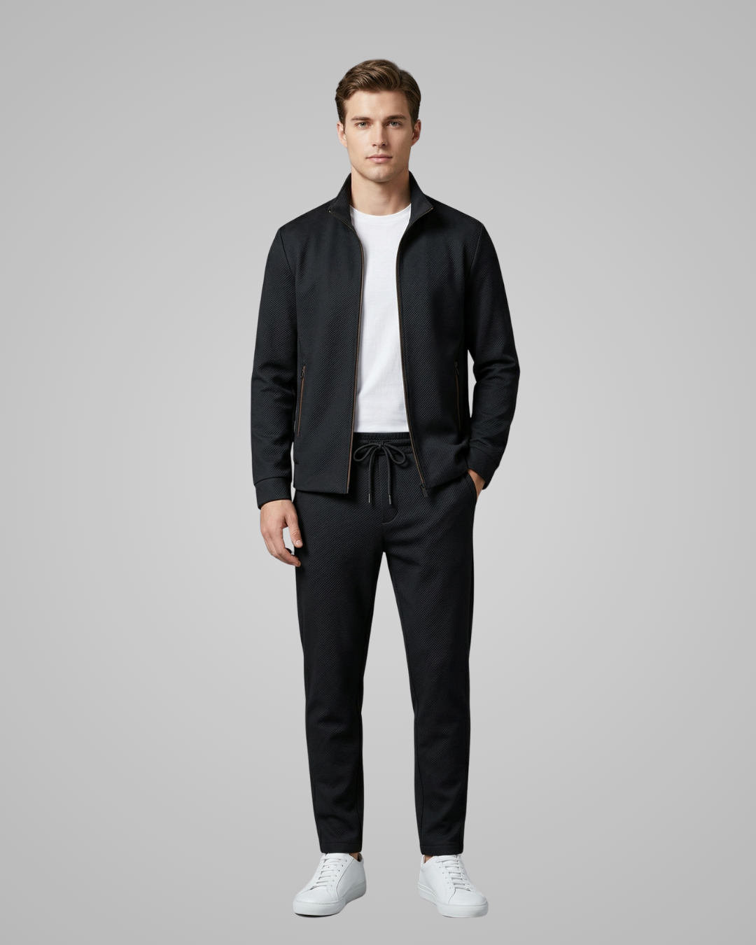 Man wearing a black jacket and pants with a white shirt on a gray background