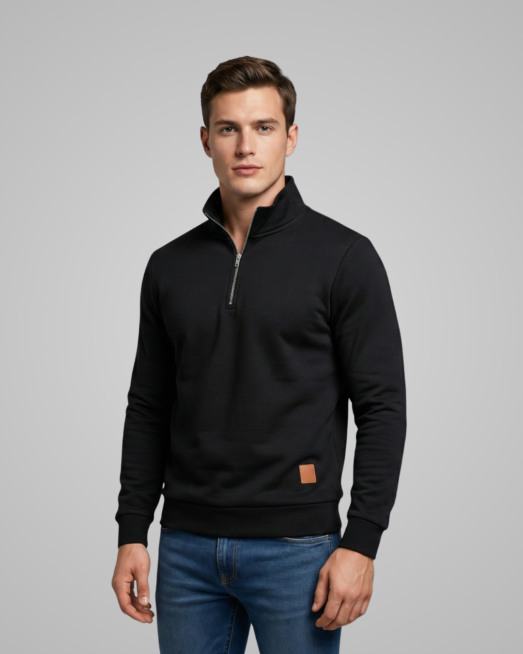 Man wearing a black quarter-zip sweatshirt with a brown patch on a gray background