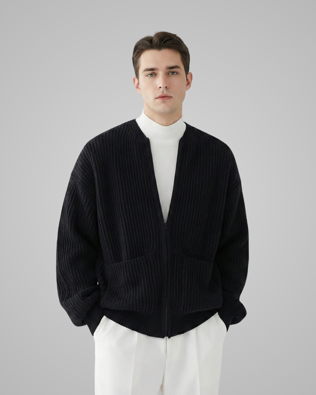 Man wearing a black ribbed sweater over a white shirt on a gray background
