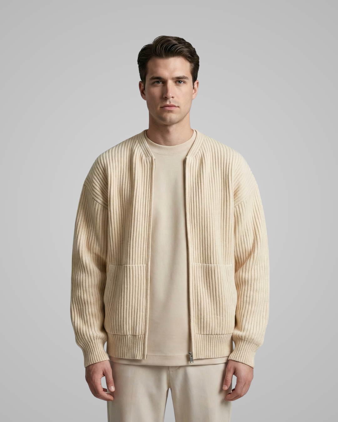 Man wearing a beige ribbed sweater over a plain shirt on a gray background