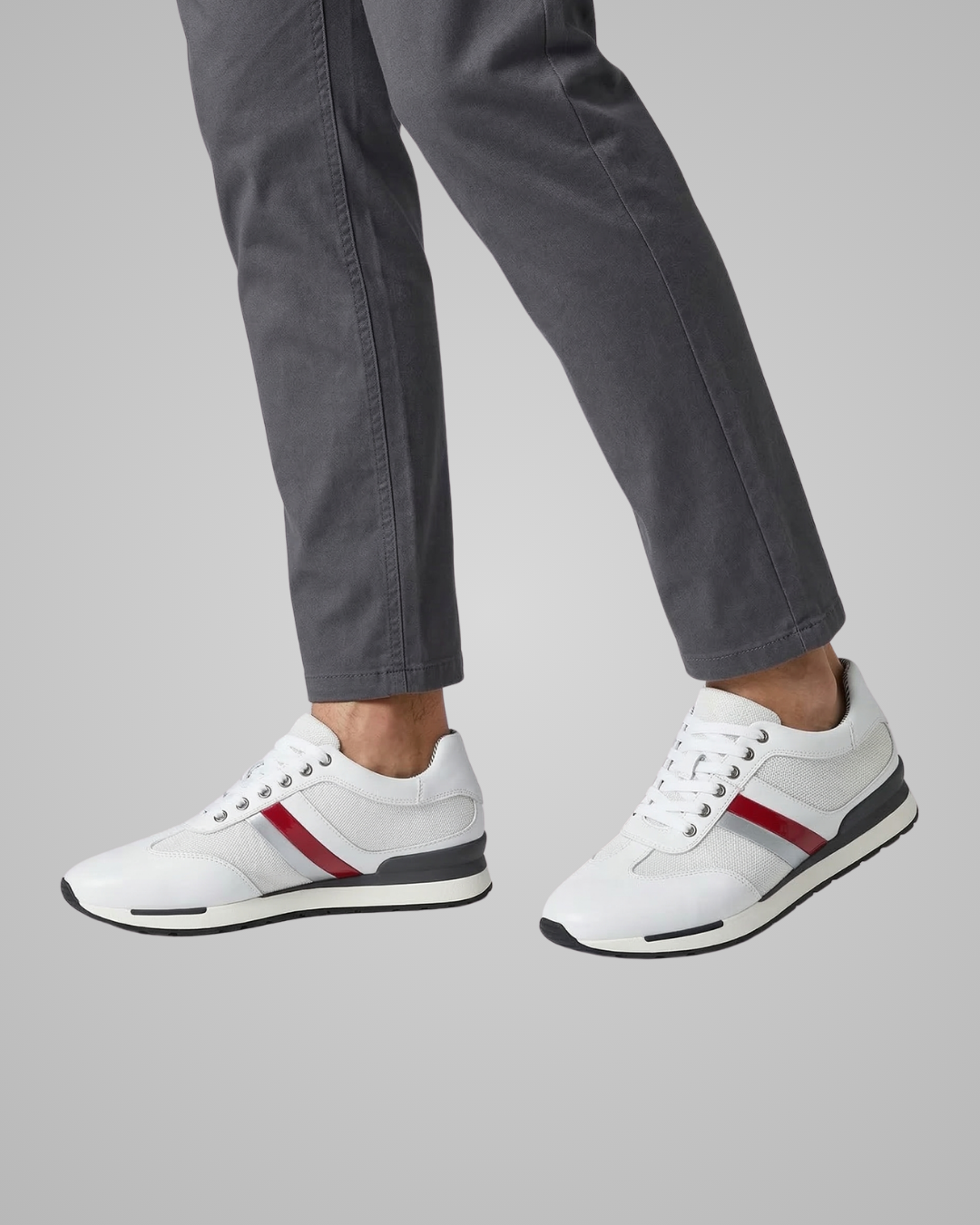 White sneakers with red accents worn by a person on a gray background