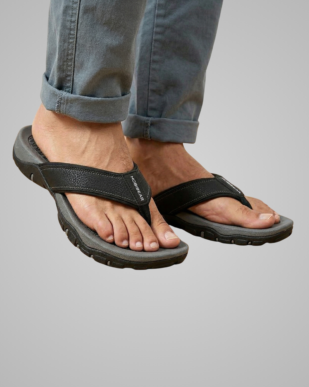 Black sandals worn with rolled-up jeans on a gray background