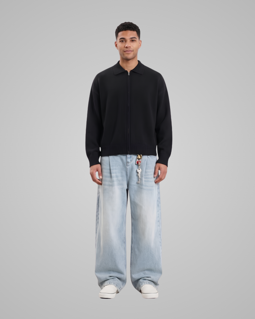 Man wearing a black sweater and light blue jeans on a gray background