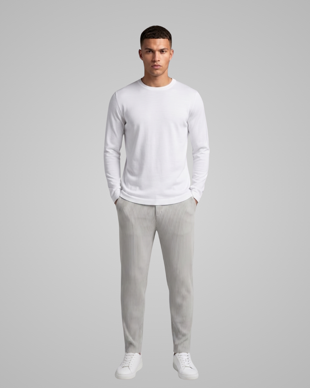 Man wearing a white long-sleeve shirt and gray striped pants on a gray background