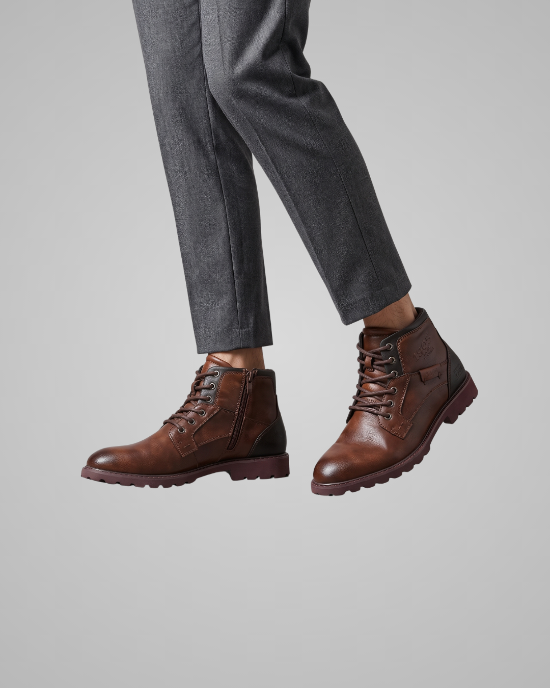 Brown leather boots worn with gray pants on a light gray background