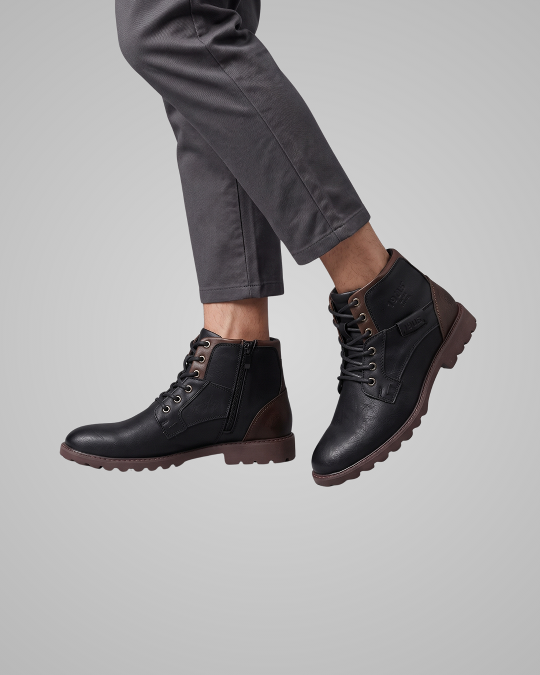 Black leather boots worn with gray pants on a light gray background