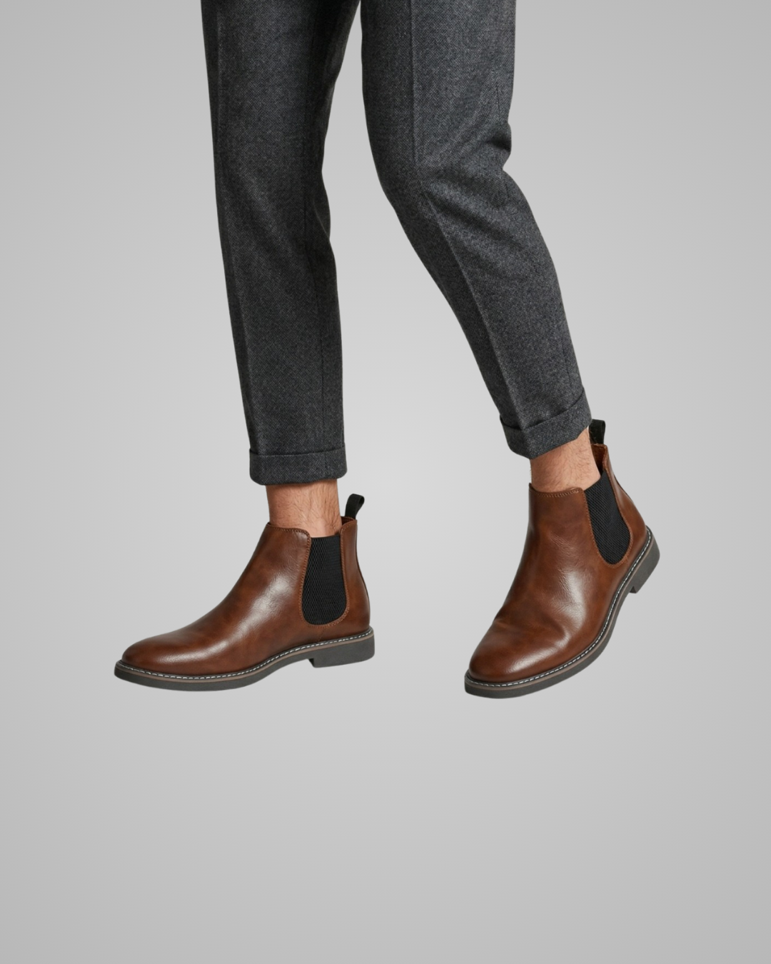 Brown Chelsea boots worn with gray pants on a light gray background
