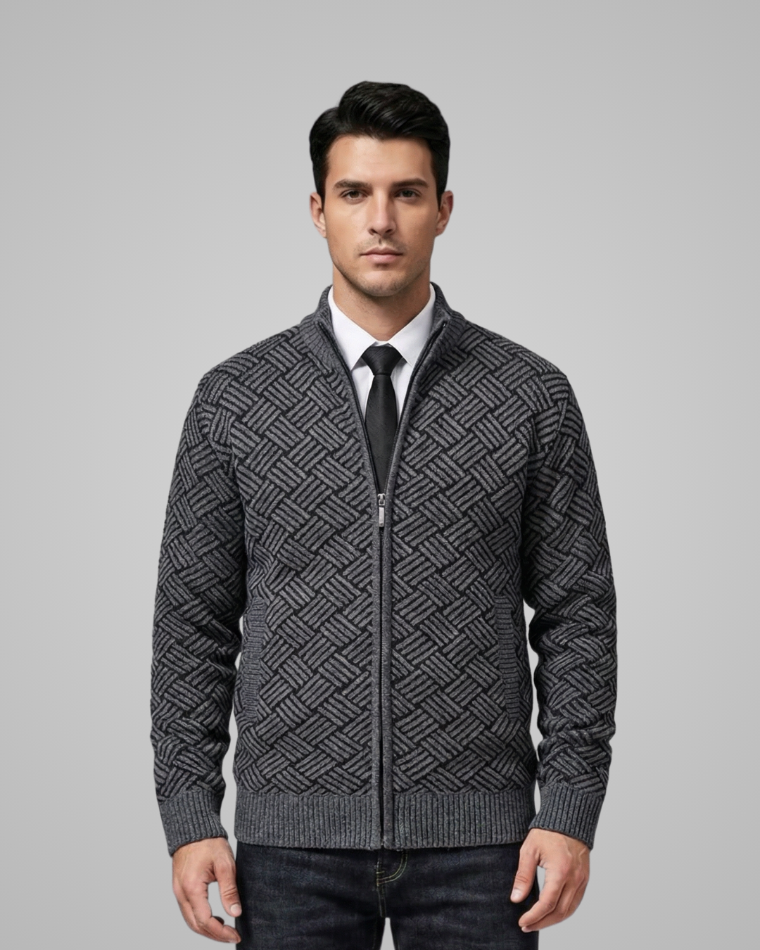 Man wearing a patterned gray sweater over a white shirt with a black tie on a gray background