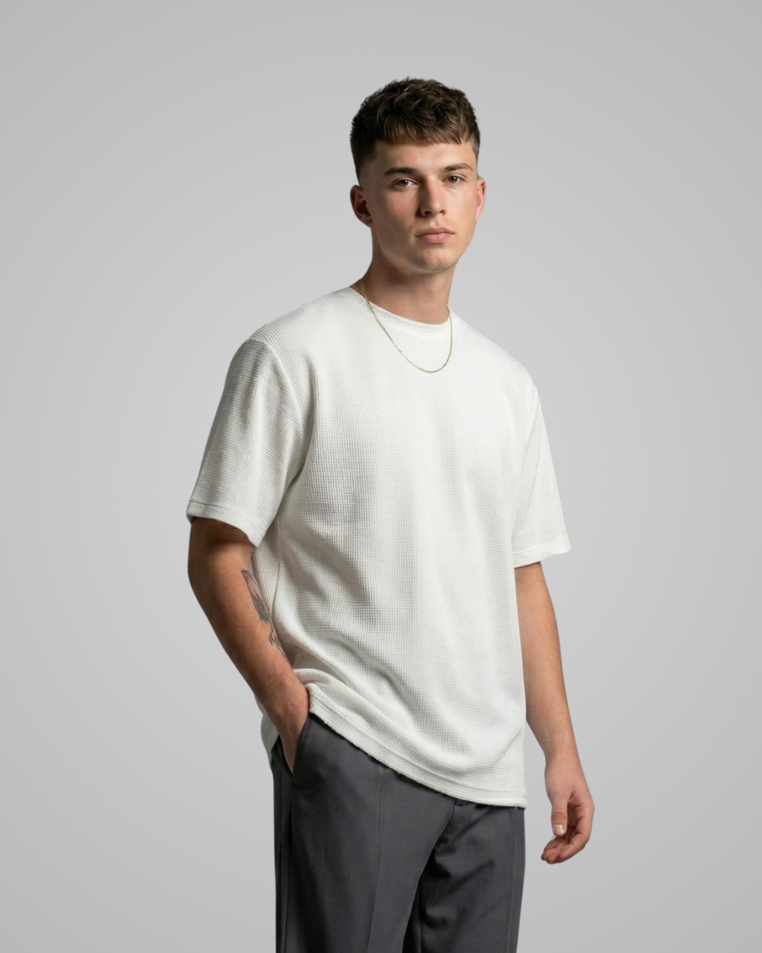 Man wearing a white t-shirt and gray pants against a plain background