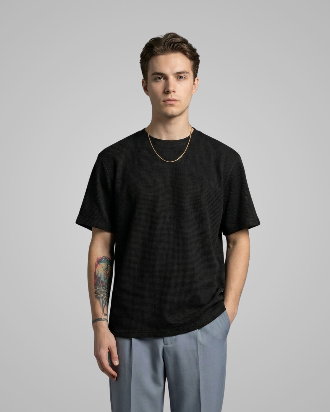 Man wearing a black t-shirt and light gray pants on a gray background