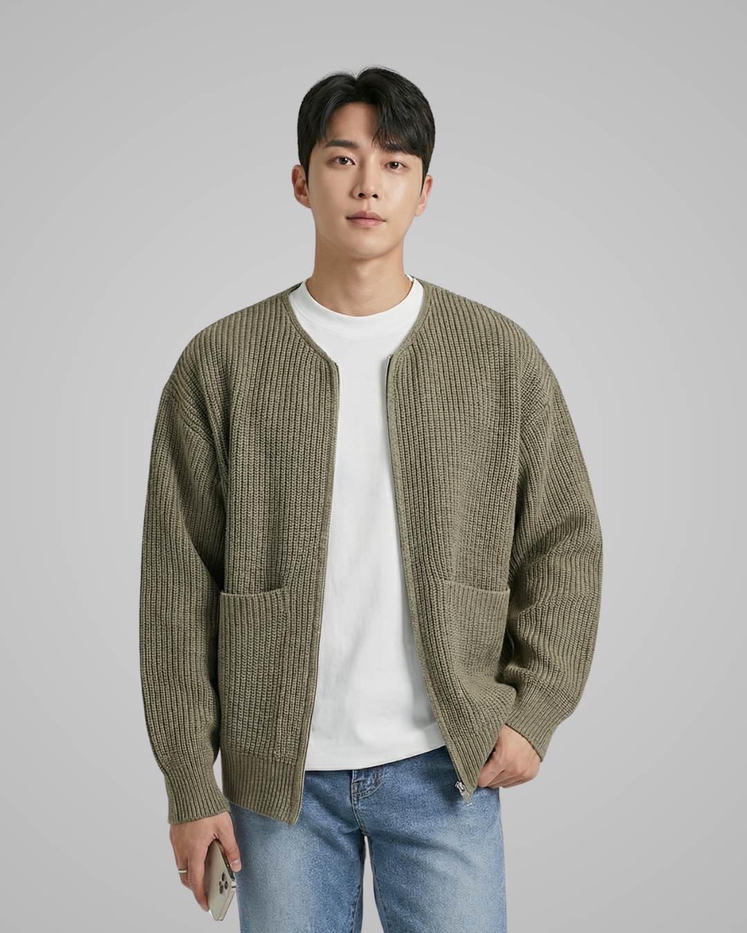 Man wearing a green knitted cardigan over a white shirt with blue jeans on a gray background