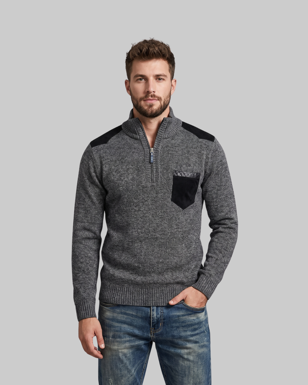 A man wearing a gray quarter-zip knit sweater with black shoulder and chest pocket accents, paired with blue jeans, against a solid gray background.