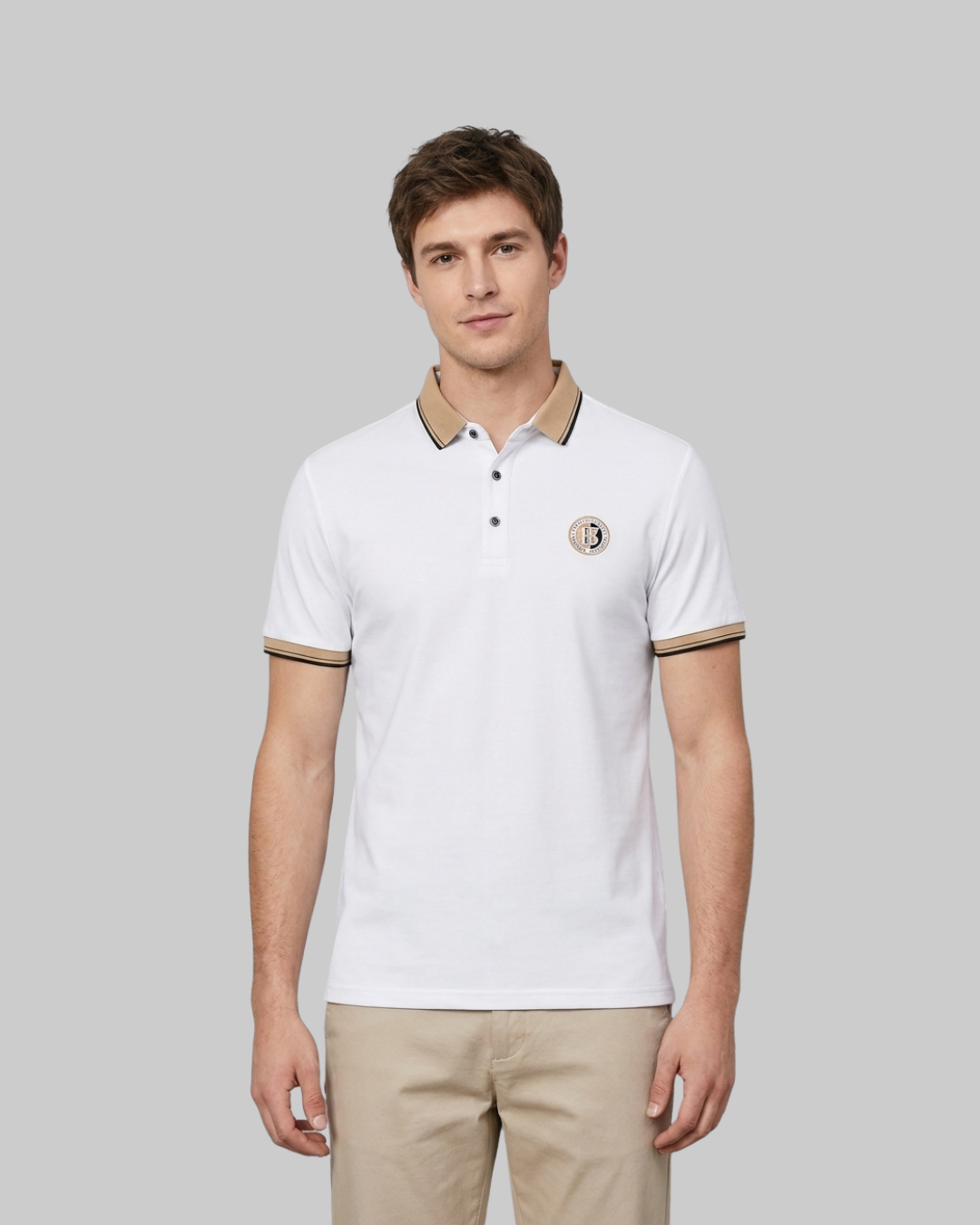 A man wearing a white short-sleeve polo shirt with beige and black trim on the collar and sleeve cuffs, paired with beige trousers, against a solid gray background.