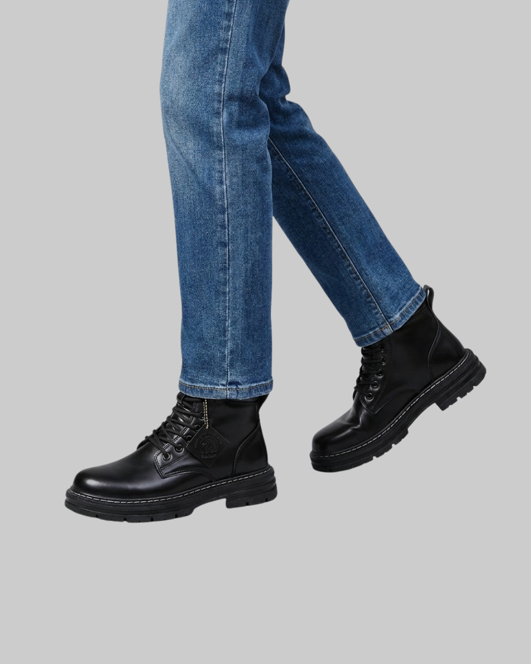 A person wearing blue jeans and black lace-up ankle boots, shown from the calves down against a plain light gray background.