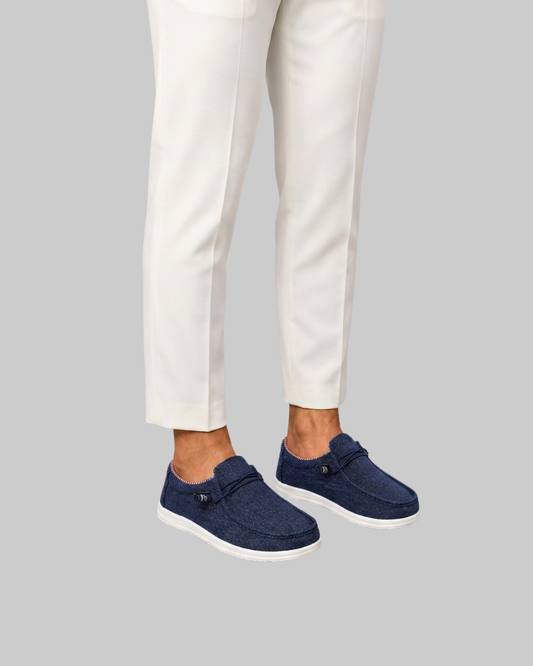 A person wearing off-white trousers and navy slip-on shoes with white soles, shown from the knees down against a plain light gray background.