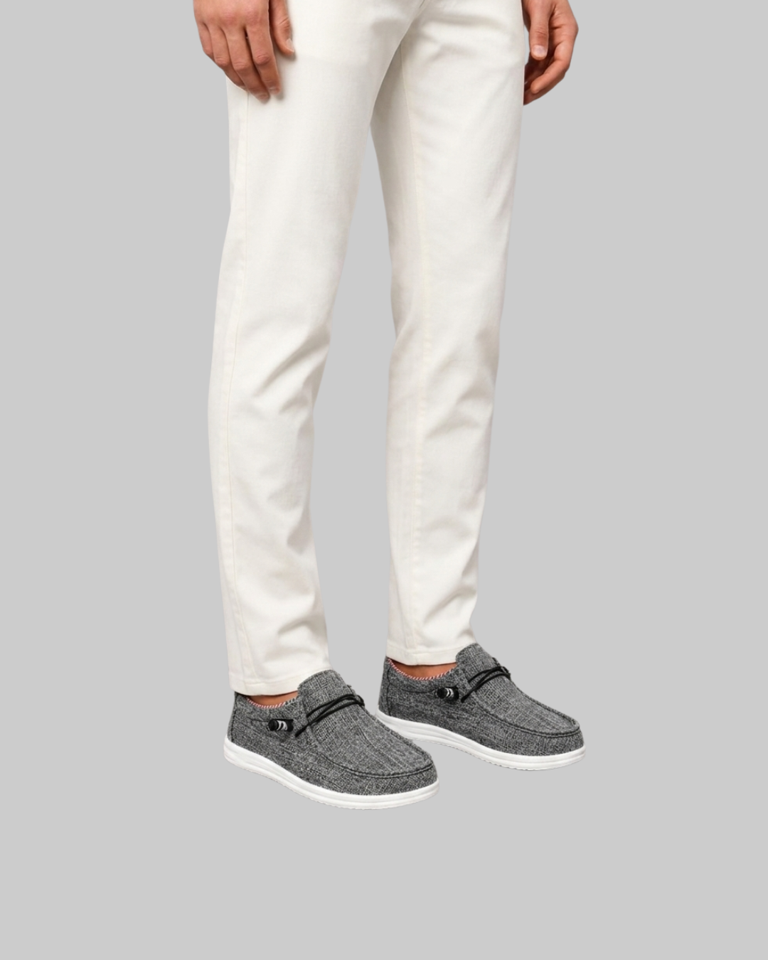 A person wearing slim-fit off-white trousers and gray knit slip-on loafers with white soles, shown from the waist down against a solid gray background.