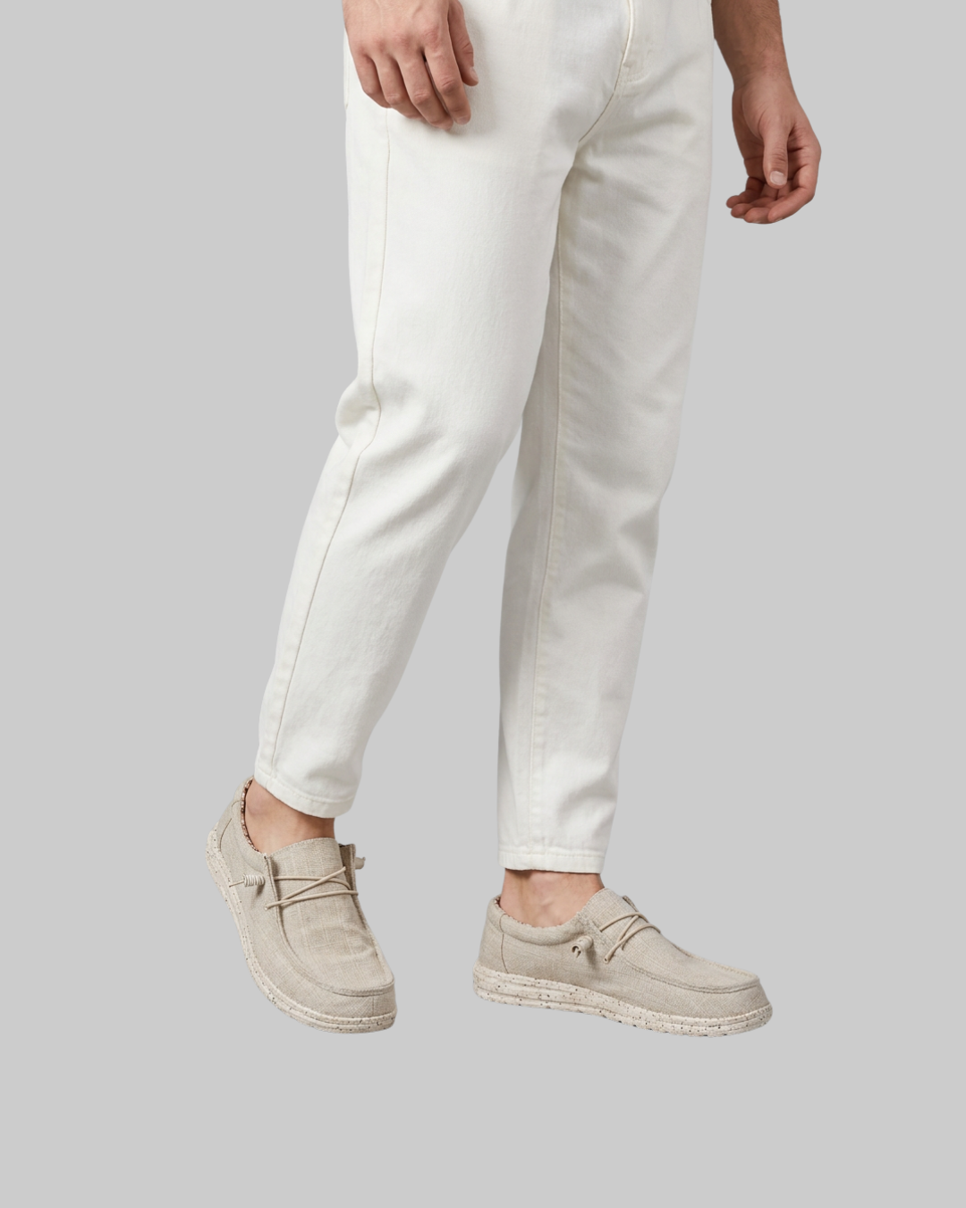 A person wearing off-white slim-fit jeans and light beige suede loafers with braided jute soles, shown from the waist down against a solid gray background.