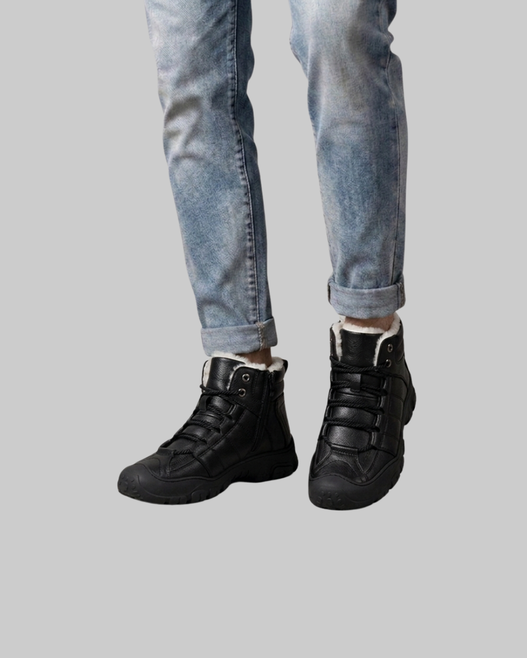 A person wearing black high-top lace-up boots with white fleece lining, paired with light-wash blue jeans, shown from the calves down against a solid gray background.