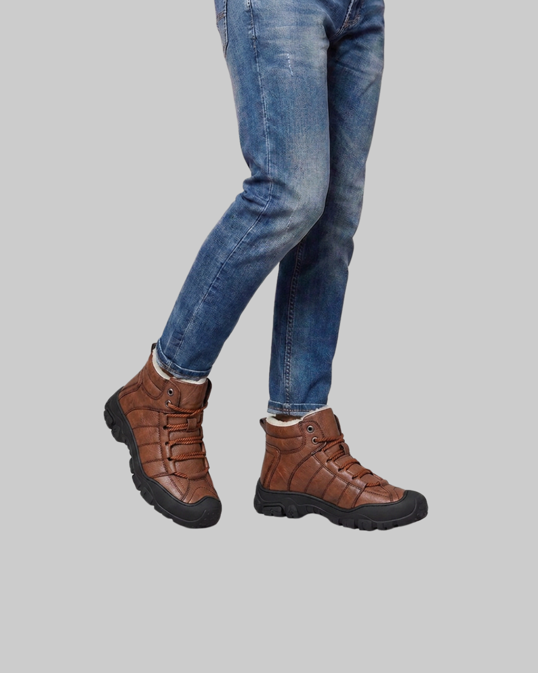 A person wearing brown lace-up ankle boots with black soles and blue jeans, shown from the knees down against a solid gray background.