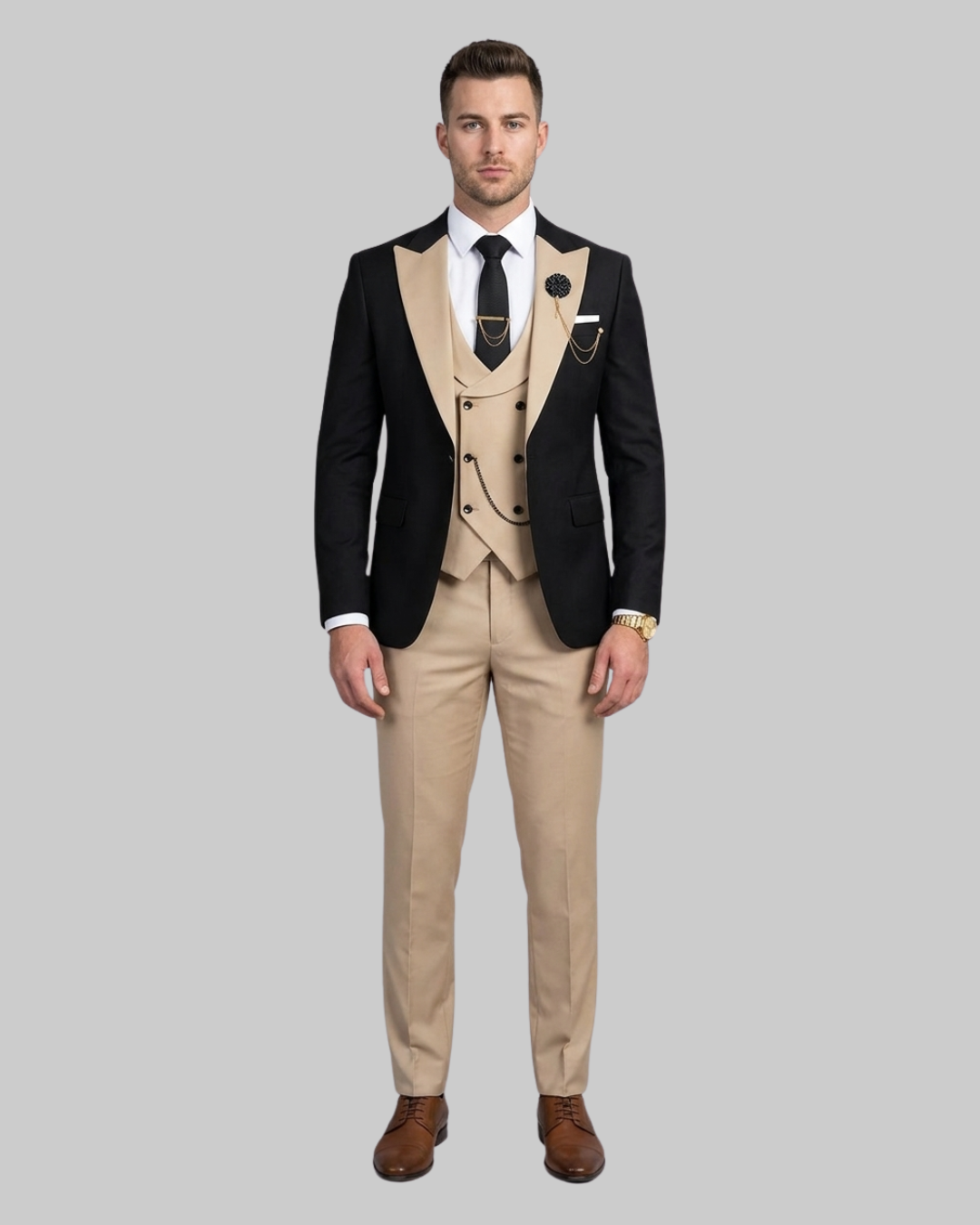 A man modeling a three-piece formal suit featuring a black blazer with peak lapels, a beige double-breasted vest, matching beige trousers, a white dress shirt, and a black tie, set against a solid gray background.