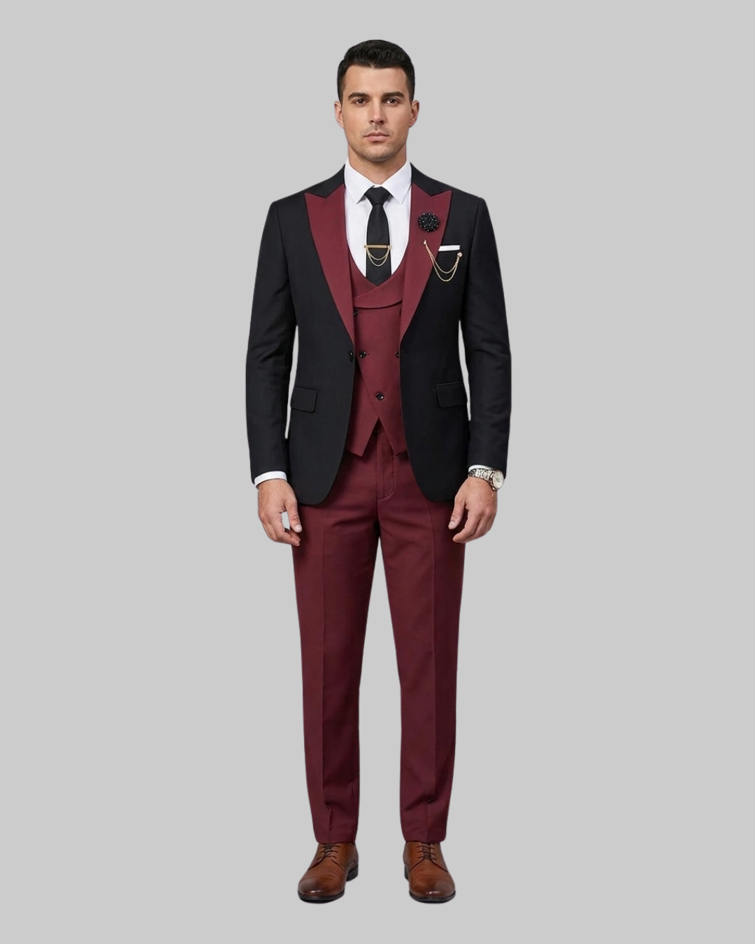 A man modeling a three-piece suit with black peak lapels and a burgundy double-breasted vest and trousers, styled with a white shirt, black tie, and brown dress shoes against a solid gray background.