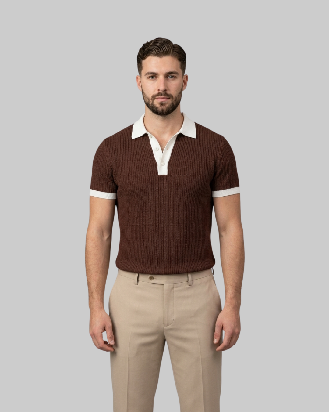 A man wearing a brown ribbed short-sleeve polo shirt with a white collar and sleeve trim, paired with beige trousers, standing against a solid gray background.