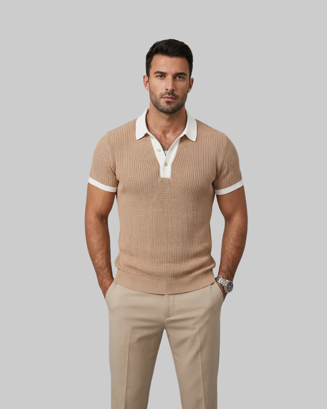 A man modeling a beige ribbed short-sleeve polo shirt with a contrasting white collar and sleeve cuffs, paired with beige trousers, against a solid gray background.