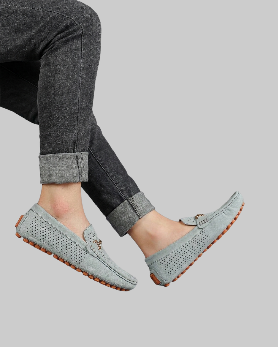 A person wearing light blue perforated moccasin-style loafers with rolled-up dark gray jeans, shown against a plain light gray background.