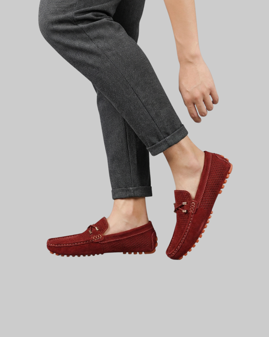 A person wearing dark gray cuffed jeans and red suede driving loafers, shown from the waist down against a solid gray background.