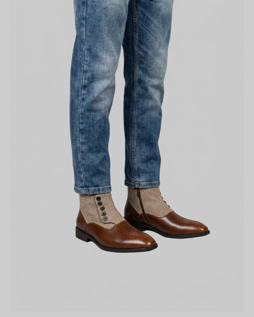 A person wearing blue jeans, beige knit socks, and brown leather lace-up shoes with brogue detailing, shown from the calves down against a light gray studio background.
