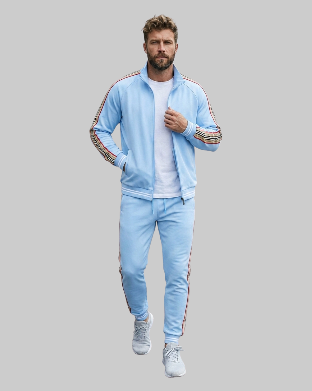 A man modeling a light blue tracksuit set consisting of a zip-up jacket and matching pants, featuring striped details on the sleeves and legs, worn over a white t-shirt and white sneakers, set against a solid gray background.