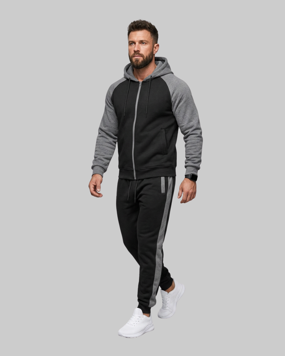A man modeling a two-tone gray and black zip-up hoodie and matching black sweatpants with gray side stripes, set against a solid gray background.